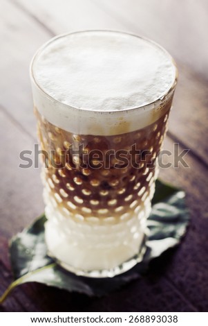 Frothy, layered cappuccino in a clear glass mug on wooden table