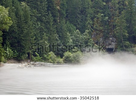 Fog rolls over a mountain lake, boat dock and tunnel in the background