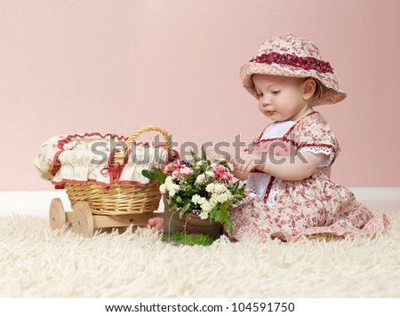 little child baby girl  indoors in baby room playing on the floor with flowers