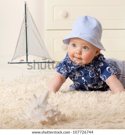 little child baby boy lying on the floor carpet indoors in baby room smiling hat clothing fashion