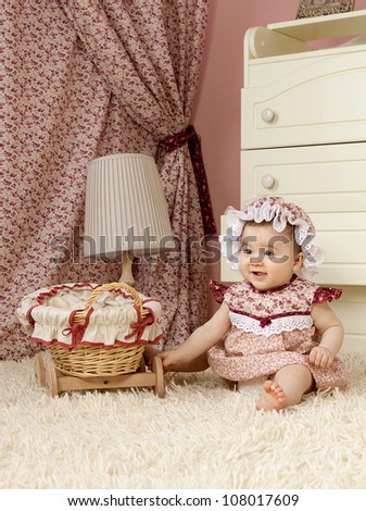 little child baby girl sitting on the floor indoors in baby room smiling  hat dress fashion