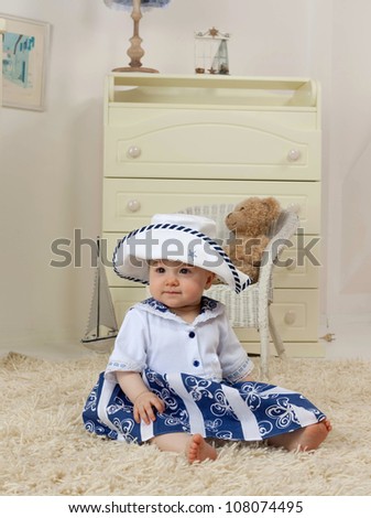 little child baby girl sitting on the floor indoors in baby room   hat dress fashion