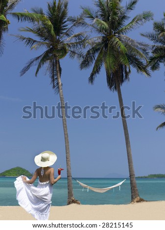 Woman in hat and white dress on the beach with cocktail