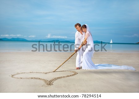 stock photo beautiful couple on the beach in wedding dress drawing heart