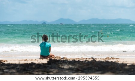 Girl sitting alone on sandy beach doing sand play
