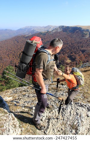 Man giving helping hand to friend to climb mountain rock cliff
