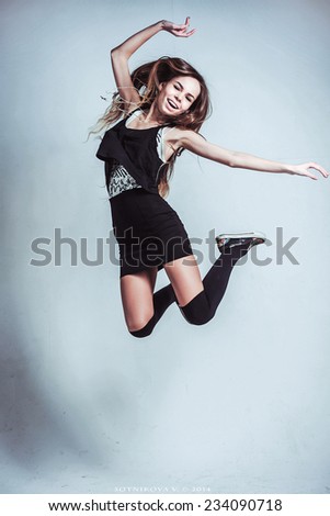 Smiling woman is jumping on gray background with flowers