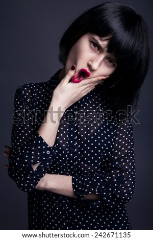 Beautiful cute woman in a black wig and the black shirt  polka dot. Perfect makeup. Closeup. Pink lips. Grey background.