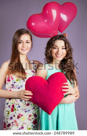 Brunet and blond cheerful young women with pink balloon hearts in blue and white dress. Beauty portrait, perfect makeup. Valentine\'s Day. Long chic curly elegant hair. Smiling girls. Closeup. 8 march