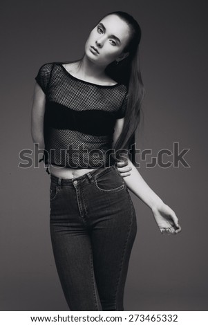 Blond cheerful young woman. Beauty portrait, perfect makeup. Long chic elegant hair. Model tests. Cute girl in black top and jeans. Isolated. Gray background. B/W