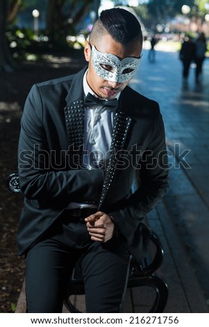 handsome man attending a masquerade ball sitting on a bench and hiding something in his pocket