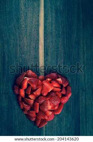 Heart-shaped strawberries on a wooden kitchen board resembling a heart locket, usable for food photography.