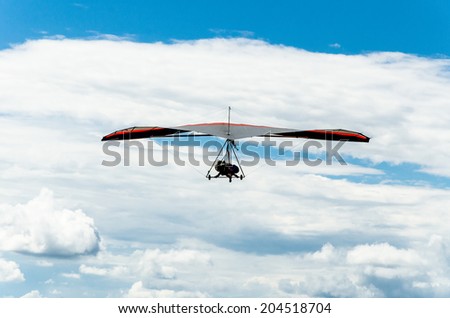Hang glider flyiing in blue sky with clouds