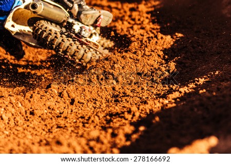 Detail of a motorcycle making a turn in dirt track with flying debris