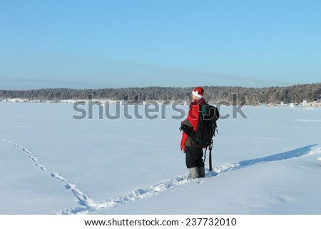The man with a backpack in Santa Claus\'s suit going on a snow field against the sky