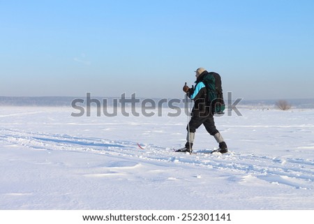 The man the traveler with a backpack skiing on snow cover of the river