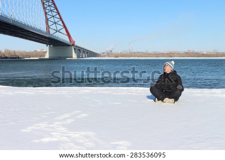 The woman practicing yoga at the bridge on the snow-covered river coast in the spring