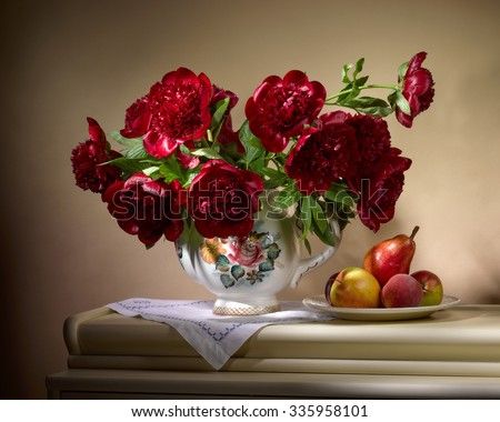 bouquet from red peonies in ceramic vase with plate of apples and pear on table on beige background