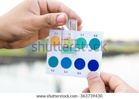 Worker use hands holding test tube with pH indicator comparing color to scale from water in shrimp pond