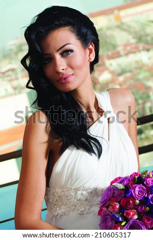 Close up portrait of beautiful young bride with long black hair. White dress, wedding bouquet of roses.