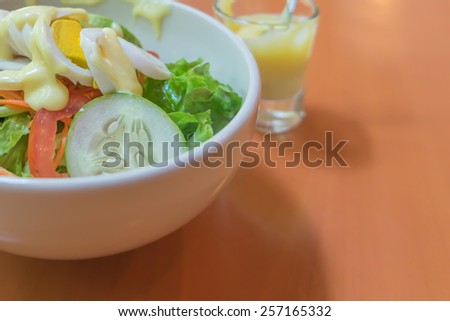 Boiled egg salad ingredients with boiled eggs, lettuce, tomatoes, carrots, cucumbers. It served on a white bowl and a little glass of dressing.