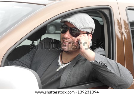Happy male driver smiling while sitting in a car with open front window and talking over mobile phone. Selective focus.