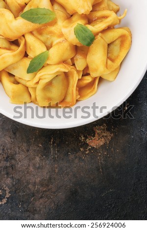 Vertical Shot of Cooked Tortellini in a White Bowl on a Dark Background. From Above, with Copy Space.