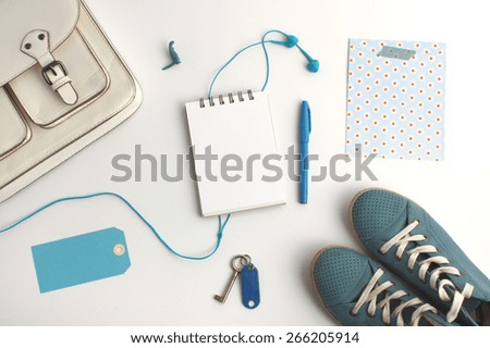Top view of bag content accessories collection in blue color theme with bag, shoes, pen, blank notepad, paper tag,headphone and keys