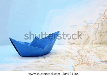 Travel concept - blue folded paper boat on map with ocean