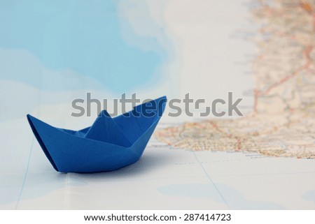 Filtered image of blue folded paper boat on map - summer sail vacation concept