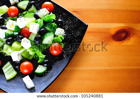 Tasty Greek salad dressed with olive oil and rosemary on wooden table with copyspace for text