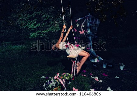 Beautiful fairy girl on the swing in the night forest