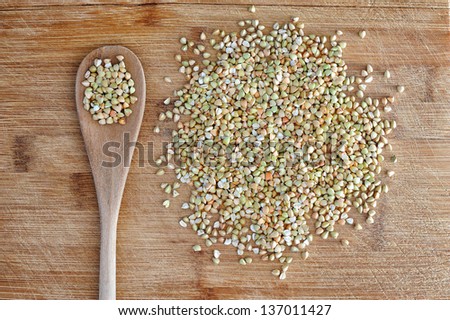 Still-life with tablespoonful of organic green buckwheat on wooden table
