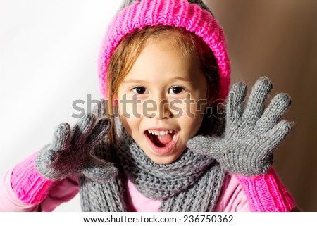 Little girl in winter hat with gloves and scarf on a white background.