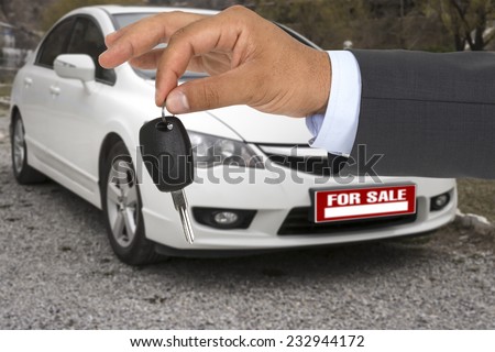 Salesman giving car keys with the car  for sale on background.