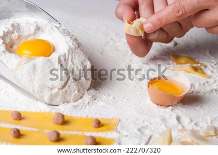 Handmade tortellini recipe, hands making tortellini fresh pasta, eggs and flour on a kitchen table
