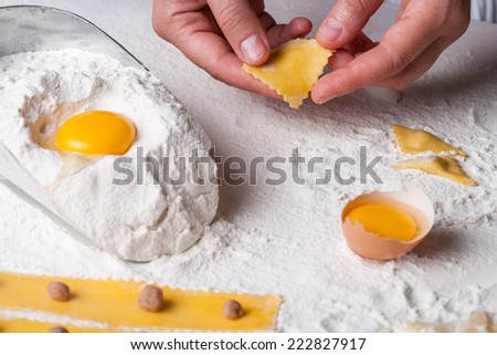 Handmade tortellini recipe. hands making tortellini fresh pasta, eggs and flour on a kitchen table.