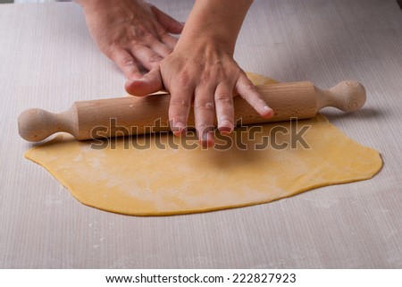 Rolled out dough, hands and rolling pin on a wood table