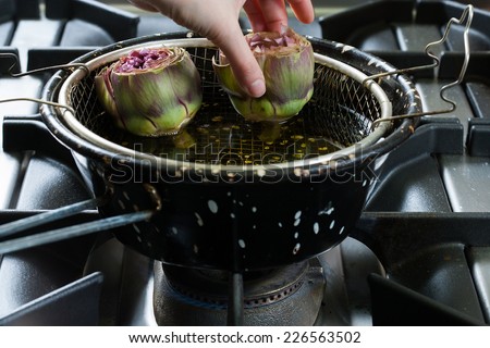 Artichokes fried in a pan of hot oil, with the grid used for frying foods.
