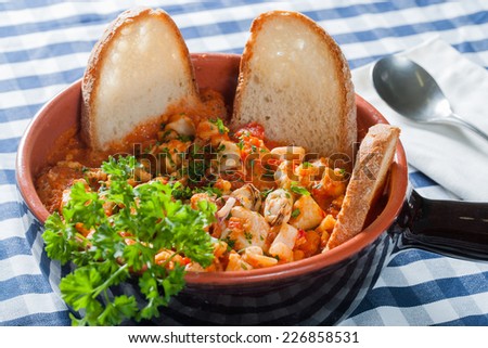 Fish soup with croutons and parsley bayonet in terracotta bowl on checkered tablecloth