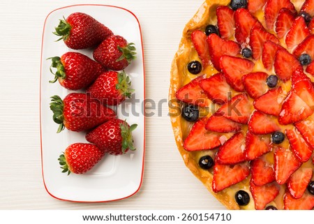 Strawberry and blueberry cake on wooden white background. Composition with white and red dish full of red fruits