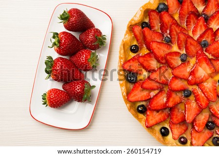 Strawberry and blueberry cake on wooden white background. Composition with white and red dish full of red fruits