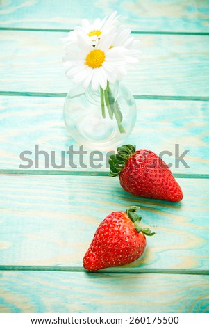 vase of daisies and two straw berry on a turquoise wood table