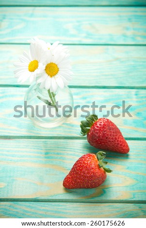 vase of daisies and two straw berry on a turquoise wood table