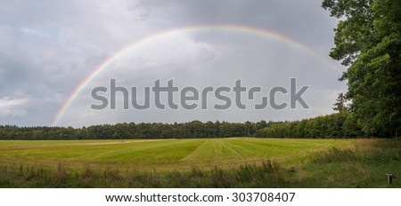 Full rainbow panorama over a Dutch meadow against a dark cloudy sky
