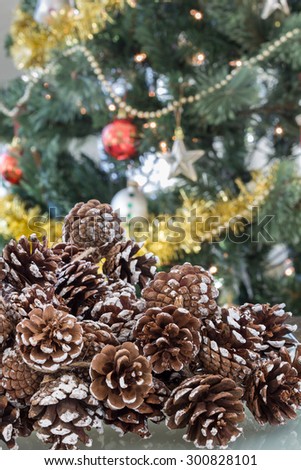 Shallow depth of field highlights a cluster of pine cones flecked with snow.  Out-of-focus, decorated Christmas tree in the background
