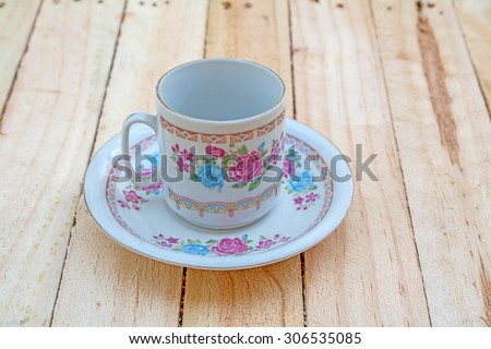 Teacup and saucer with floral rose ornament in classic style on wooden board