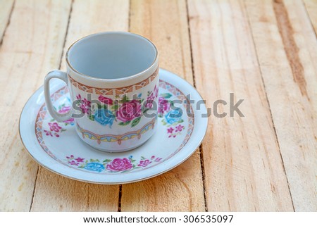 Teacup and saucer with floral rose ornament in classic style on wooden board