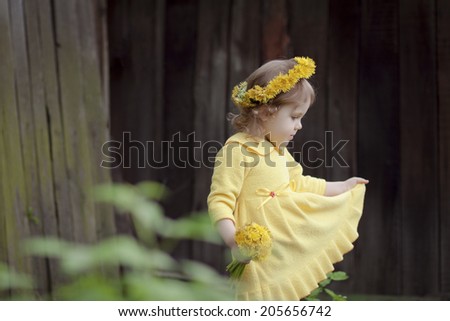 Little girl with a wreath of dandelions in a yellow dress