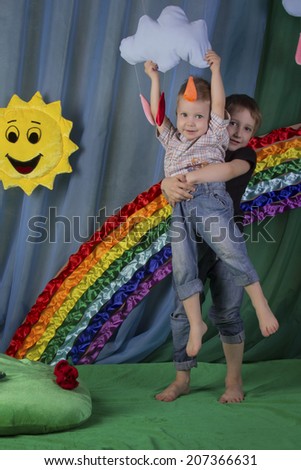 Two happy joyful boy on background of the rainbow, sun and clouds, reach for the cloud